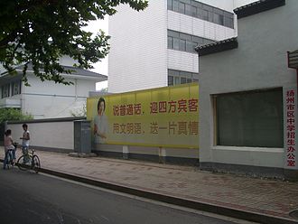 A poster outside a high school in Yangzhou urges people to "Speak Putonghua to welcome guests from all around, use the language of the civilized (Putonghua) to give your sincere feelings". Yangzhou-Highschool-Speak-Putonghua-3388.jpg