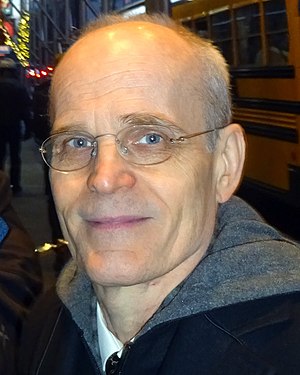 Close-up photograph of a thin bespectacled man, mostly bald with short gray hair around