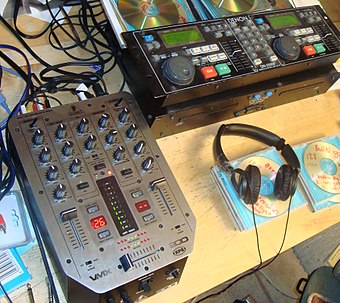 This example of a CD player used by DJs is the Denon DN-2500 dual CD player, on the right side of the picture. A Behringer VMX-200 DJ mixer is also shown in the left side, in the foreground.