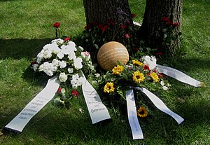 Die Gedenkkugel ist umgeben von verschiedenen Blumen und Kränzen, an denen Schleifen befestigt sind.