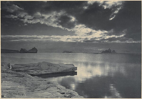 Photo of an icy shore, calm water, and illuminated clouds