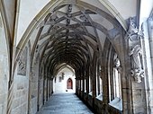 Fotografia a cores de uma das passagens de um claustro, cujas abóbadas são esculpidas.