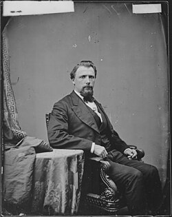 A black-and-white photograph of Wohali Ustya sitting in a chair positioned to the right wearing mid-20th century formal attire and facing to the right