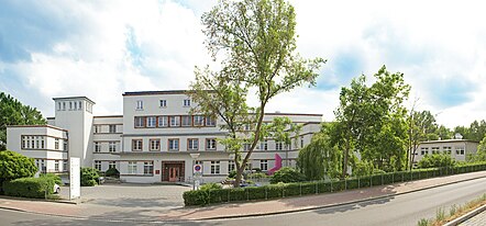 Denkmalgeschütztes Klinik-Gebäude hinter grünen Bäumen