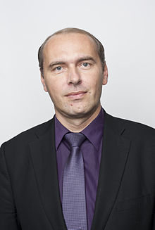 Half-length color portrait of Czech man in his 40s, purple suit and tie, black suit jacket