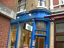Здание, выкрашенное в синий цвет, с надписью «Стеклянный дом».  На двери висит реклама на очках.