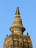 Üstte altın metal koni şeklinde bir finial ile kesilmiş bir piramidin tepesindeki Mahabodhi tapınağının zirvesinin fotoğrafı, arka plan açık mavi bir gökyüzü