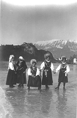 Skupina žensk v gorenjski narodni noši na drsalkah, pozira na zamrznjenem Blejskem jezeru 1909-14.jpg