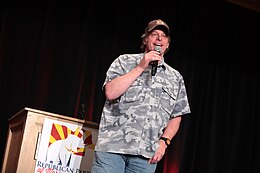 Homme costaud en chemise de camouflage prononçant un discours