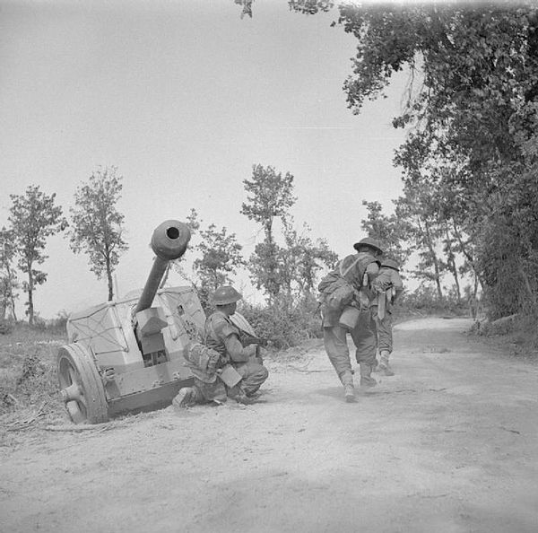 Men of 'A' Company of the 5th Battalion, Queen's Own Royal West Kent Regiment advance along a road past an abandoned German 75mm anti-tank gun in the 