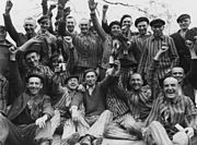 Dachau survivors toast their liberation as the man standing in center between the bottles wears a P triangle.