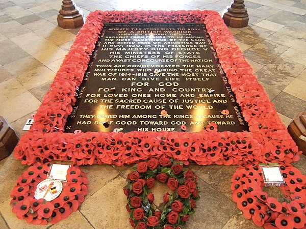 A black tombstone surrounded by red poppies with three wreaths at its foot.