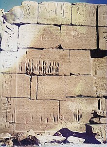 A stone wall that has eroded so that the joints between blocks are exposed. The blocks have straight edges but uneven shapes.