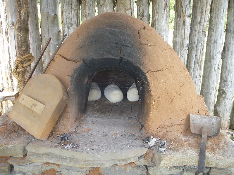 Old primitive traditional Moroccan outdoor earth clay oven made of  sandstone and mud, a fire burns inside and smoke rises from a hole in the  top. Architecture Stock Photos