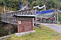 Eine mit bunten Gebetsfahnen behängte Brücke ins Wildschutzgebiet Bumdeling, wie ein daneben stehendes Schild zeigt