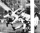 photo en noir et blanc d'un match de football, deux joueurs luttent devant les cages pendant que la gardien plonge