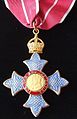 insignia of a Commander of the Order of the British Empire (CBE, here with military ribbon). A similar medal is also worn as part of the insignia of a Knight Commander or Dame Commander (KBE or DBE)