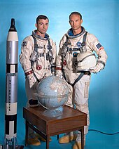Photographie de Young et Collins en combinaison Gemini à côté d'une maquette de leur fusée et d'un globe terrestre.