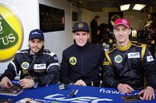 Zdjęcie trzech kierowców wyścigowych, widzianych z przodu, w czarno-złotych kombinezonach.