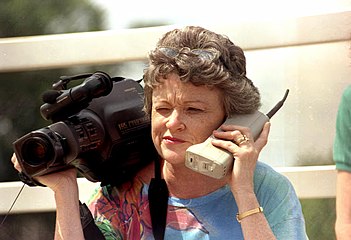 Journalist Lucy Morgan holding one of the very first brick mobile phones, as well as a 1980s video camera