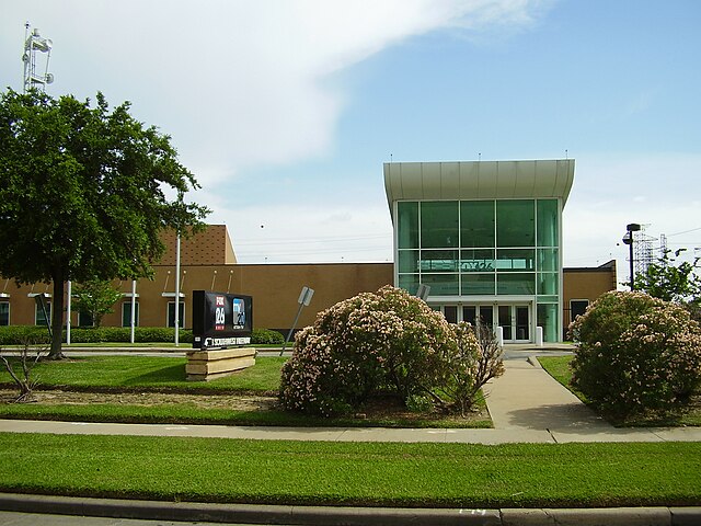A stucco and glass building with a sign outside bearing the KRIV and KTXH logos.