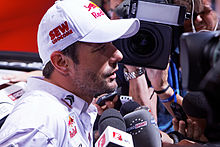 Sébastien Loeb i profil med hette, omgitt av mikrofoner til flere journalister.