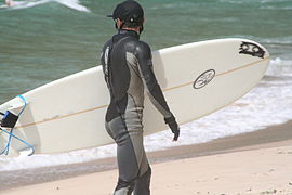 Surfer in wetsuit carries his surboard on the beach