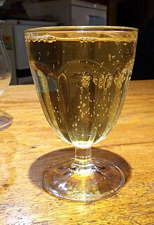 Photographie d'un verre avec une boisson pétillante jaune clair.