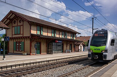 Silver-and-green train passes two-story building with gabled roof