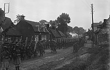 Elements of the 2nd Division, the 1st Battalion Irish Guards, march through a French village during 1915. 2nd Div First World War, Q 28870.jpg