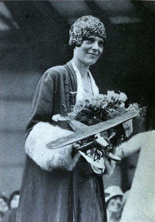 Amelia Earhart holding flowers and a model of the Friendship, presented by a Boston scholboy