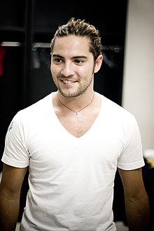 A man looking to the right, wearing a white shirt and red cloth collar Charm in gold.