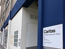 Moderne Haus-Fassade in weiß-blau mit dem Caritas Schild.