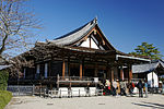 Wooden building with open railed veranda, gabled roof and an attached step canopy.