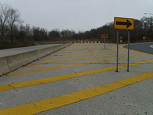 A freeway coming to a blocked-off deadend in a wooded area, with a right arrow sign pointing motorists onto an offramp