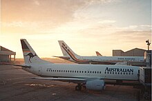 An Australian Airlines Boeing 737-300 at a gate at Sydney Airport, with a company Airbus A300 in the background, in TAA colors, 1987 Sydney Kingsford Smith Airport at dawn 19th June 1987.jpg