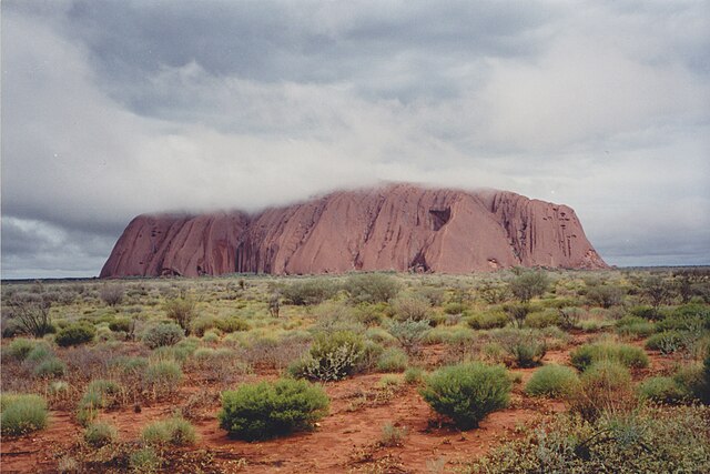 De Uluru fahlbruun mit wulcheverhülltem Gipfelplateau (Blick us Nordweste).