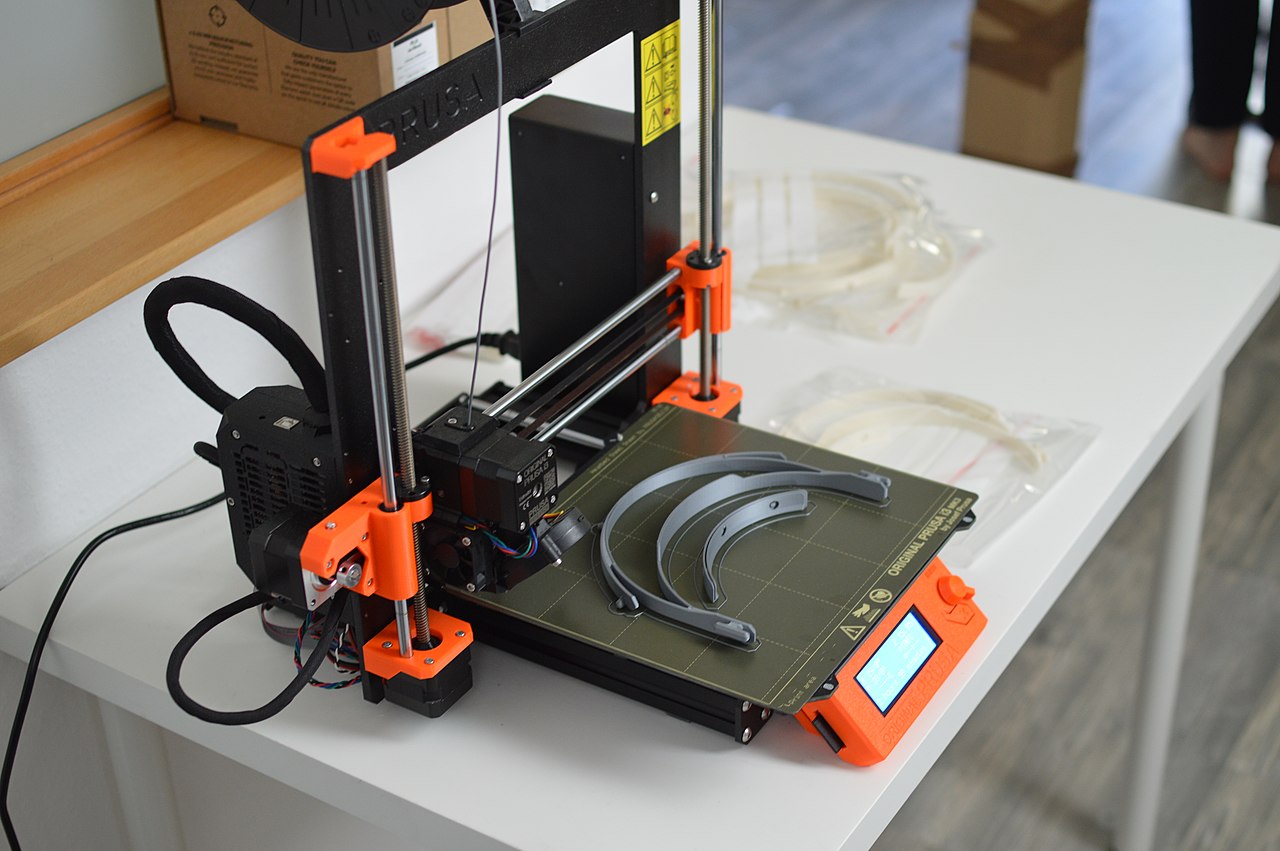 An image of a Prusa Mk3 printer with completed objects on the build plate and filament in the extruder