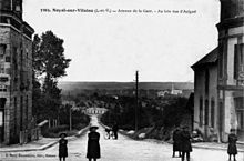 Postal antigua de la avenue de la gare en Noyal-sur-Vilaine con al fondo el edificio de pasajeros de la estación de Noyal-Acigné y más adelante el pueblo de Acigné.