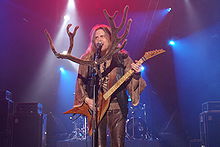 Pria berambut panjang krem, kemeja dengan lengan lebar dan coklat rompi kulit dan celana, memainkan gitar di atas panggung dan bernyanyi. Ada banyak pasangan merasa tanduk disematkan ke mikrofon.