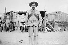 Photographie en noir et blanc d'un soldat se tenant debout, portant un sombrero et des cartouchières.