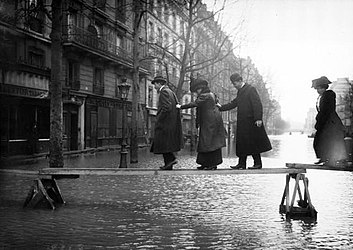 Pedestrians traversing planks over the floodwaters.