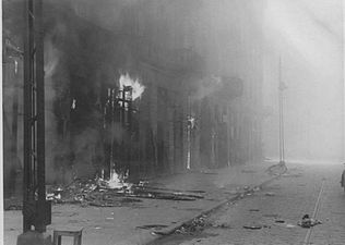 IPN copy #48 (No image caption, in section This is how the former Ghetto looks after having been destroyed) Zamenhofa Street between Wołyńska and Miła looking North, with burning Zamenhofa 29, 31 and 33 on the left.