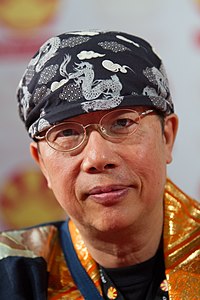 Profil von Toshio Maeda, der die Kamera mit Brille und dunkelblauer gemusterter Kopfbedeckung betrachtet.
