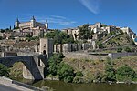 Ville avec églises et autres grandes structures sur une colline près d'une rivière.