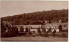 Kırsal alanda demiryolu raylarının yanında büyük bir fabrikayı gösteren bir kartpostal