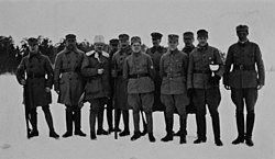 Mustavalkoinen kuva, jossa 11 sotilasasuita miestä seisoo ryhmässä. Osalla Kulosaaren suojeluskuntalaisista on kivääri.