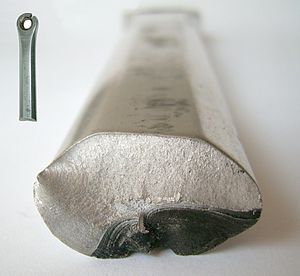 A roughly ovoid metal cylinder, viewed end-on. The bottom right portion of the metal's end surface is dark and slightly disfigured, whereas the rest is a much lighter colour and not disfigured.