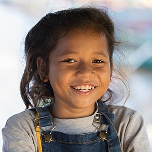 Smiling girl in sunshine wearing bib overalls in Laos at golden hour.jpg