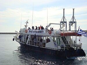 A vessel with a banner that reads "SPIRIT OF HUMANITY" and a Greek flag/ Two container cranes are in the background